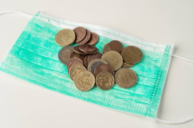 Avrupa sikkeleri yeşil koruyucu maskenin üzerinde duruyor. Tıbbi tedavi veya salgın maliyetleri ve soyut harcamalar.