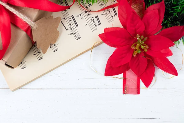 Christmas ornament and music sheet on white natural wooden table. Red ribbon bow. Poinsettia. Copy space at the bottom. Gift or present with label and twine.