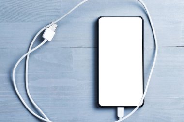 Boş ekranlı daha az akıllı telefon ve tahta arka planda güç kablosu..