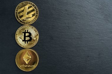 Fiziksel Bitcoin, Litecoin ve Ethereum altın sikkeleri siyah taş levha arka planında. Kripto para birimi. Boşluğu sağda kopyala.