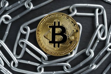 Fiziksel Bitcoin altın sikkesi karanlık taş levha arka planında kıvrımlı parlak metal bir zincir üzerinde. Kripto para birimi yasal kısıtlamaları soyut kavram.
