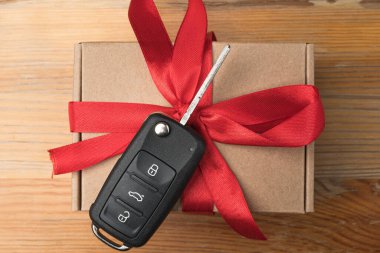 Kağıt kutuda araba anahtarı ve doğal ahşap masa arkasında kırmızı fiyonk. Noel ya da Sevgililer Günü hediyesi ya da şu anki soyut kavram.