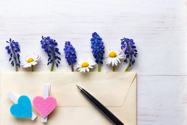 Letter, hearts, pen, scissors and delicate flowers on white natural wooden background. Classic letter correspondence abstract concept. Copy space in the top right corner.