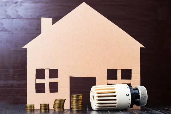 Home heat savings or expenses concept. Coin stacks, radiator regulator, house shape.