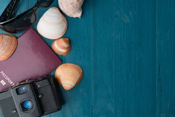 Passport, vintage film camera, sunglasses and seashells on a blue wooden background. Summer travel abstract concept. Copy space on the right.