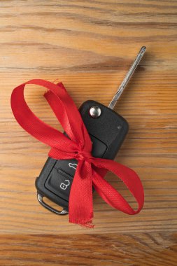 Kırmızı fiyonklu araba anahtarı, doğal ahşap masa arkasında. Noel ya da Sevgililer Günü hediyesi ya da şu anki soyut kavram. Düz üst görünüm.