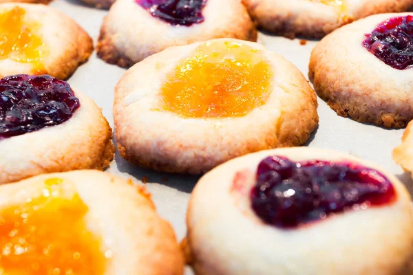 Homemade cookies filled with red and orange jelly jam on a baking paper. Domestic kitchen.