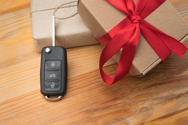 Kağıda sarılı kutular ve doğal ahşap masa arkasında kırmızı fiyonk olan araba anahtarı. Noel ya da Sevgililer Günü hediyesi ya da şu anki soyut kavram.