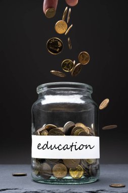 Kavanozdaki bozuk paralar ve beyaz etiketli eğitim metinleri. Kafkasyalı adam yukarıdan para atıyor. Tasarruf kavramı. Uzayı kopyala Dikey yönelim.