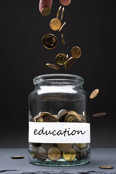 Монеты в банке с текстом образования на белой этикетке. Белый человек бросает деньги сверху. Экономит абстрактное понятие. Принято. Вертикальная ориентация
.