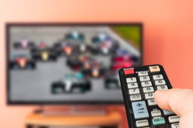 Beyaz adam evde televizyonda Formula 1 yarışını izliyor. Kanal değiştiriliyor ve sesi uzaktan kumandayla ayarlanıyor. 