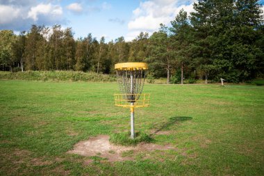 Yellow disc golf basket on a green field on a nice sunny day