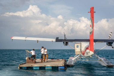 Maldivler, 10th Şubat 2018 - turistler Maldivler Hilton otelin yakınındaki bir offshore ahşap platform için bekleyen bir deniz uçağı. Mavi su, bulutlu gökyüzü, güneşli havalarda.