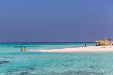 Maldives, Feb 8th 2018 - Tourists swimming in a turquoise blue sea, desert island, small traditional hut hotel on a blue sky day, paradise feeling in Maldives. clipart
