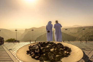 Two mans dressing with arab white clothes in a hotel in Oman. Orange predominance in the picture, feeling of desert, dry place, no clouds clipart