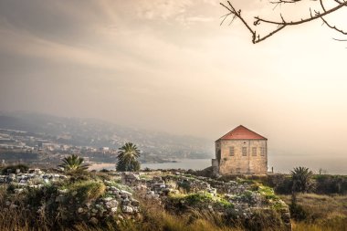 Muhteşem manzaralı Byblos, geleneksel ev, kayalar, ağaçlar, dağlar içinde belgili tanımlık geçmiş palms. Lübnan'daki Haze sıcak ışık