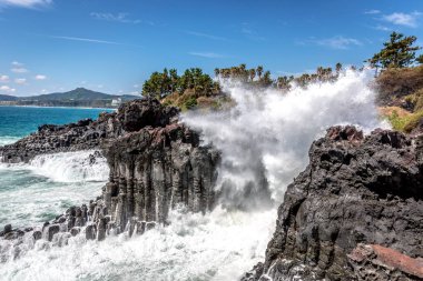 Bir dalga kırma taş karşı ve Güney Kore'de Jeju adasında havadaki su püskürtme