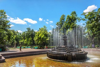 Chisinau, Moldavia - July 4th 2018 - Locals and tourists walking around a beautiful water fountain in a open air park with trees and blue sky clipart