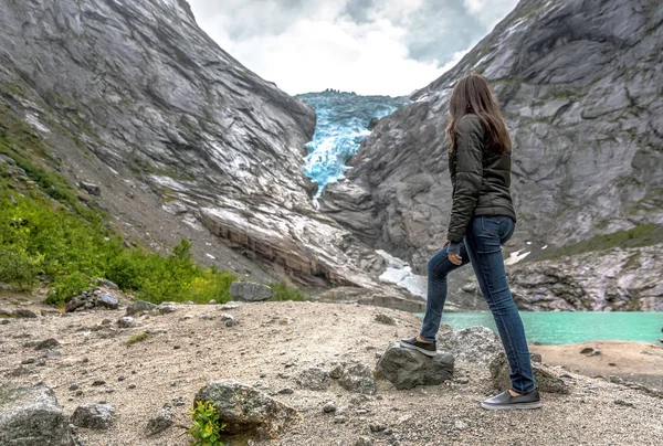 A tourist woman observing a glacier retreating among the mountains in Norway