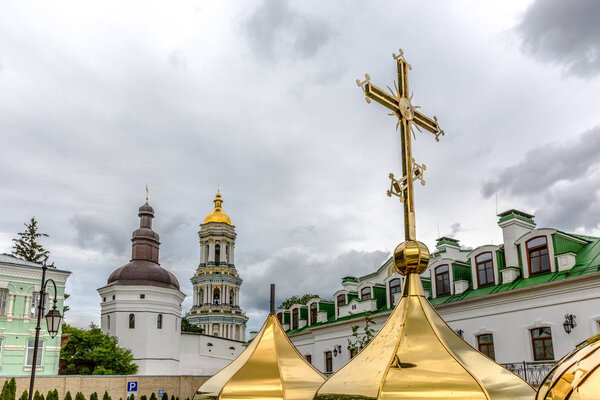 A large cross in golden color with a monastery at the background in a cloud day in Kiev, capital of Ukraine