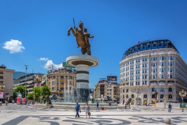 Skopje, Macedonia - July 2nd 2018 - Tourist and locals walking in front of a high horse statue with a water fountain and the Marriott hotel in a blue sky day in Skopje clipart