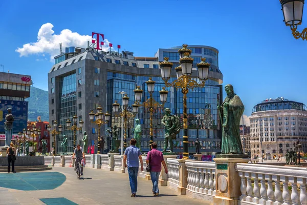 Skopje, Makedonya - 2nd Temmuz 2018 - turist heykel ve T-hareket eden Üsküp, Makedonya'nın başkentinde bir mavi gökyüzü gün'bina ile bir köprüyü geçtikten