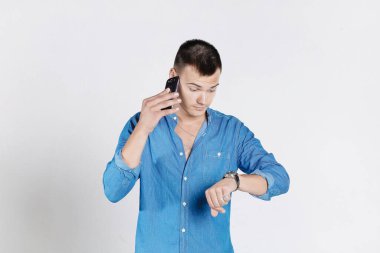 İş adamı kol saatine bakıyor ve beyaz arka planda telefonla konuşuyor..