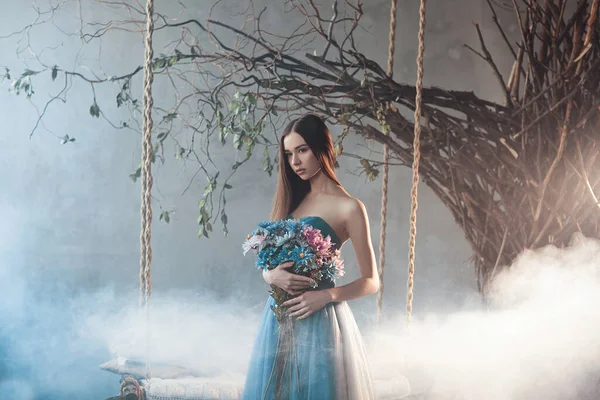 真正美丽的美丽而沉着的女人 穿着长长的雪纺蓝色连衣裙 手里拿着一大束鲜花 站在树旁的森林里摇曳着 森林里有雾 气氛异常奇妙 木柴仙女 — 图库照片