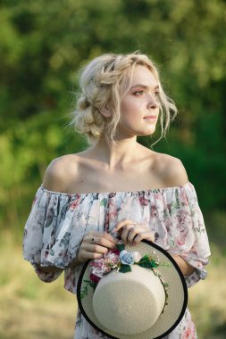 Çiçek desenli ve şapkalı, açık yaz elbisesi içinde, güzel saç stili olan hoş sarışın bir bayan resmi. Kızlar için modaya uygun bir yaz tatili. Romantik çekim..