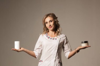 Beyazlı doktorların elinde olan iki ürün arasında akıllıca ve akıllıca bir seçim. Güzel, gülümseyen, beyaz saçlı doktor elinde beyaz arka planda iki ilaç ve krem tüpü tutuyor..