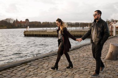 Güzel görünümlü bir çift, sıradan bir şekilde el ele tutuşup rıhtımda yürüyorlar. Şehir tarzı. Şehirde dolaşıyorum..