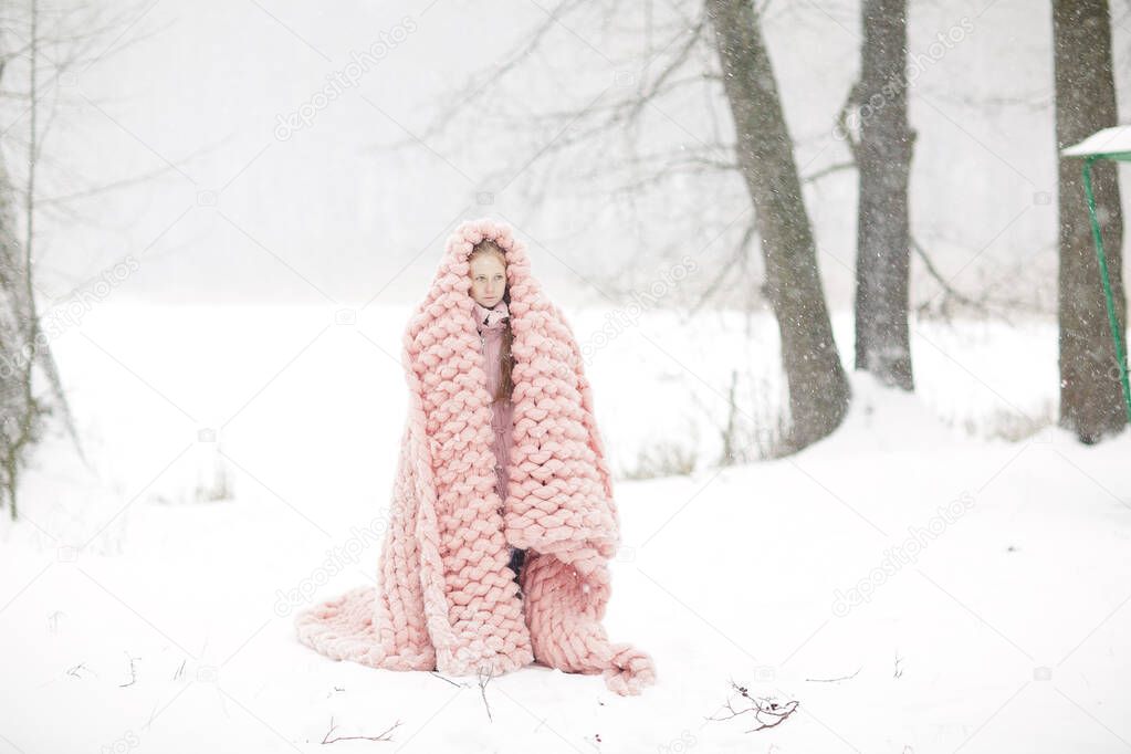 Young Beautiful Caucasian Woman in Winter Clothes and Giant Knitting Pastel Pink Blanket with Spring Flowers Walking in the Snowy Forest Dreaming About Spring White Hat