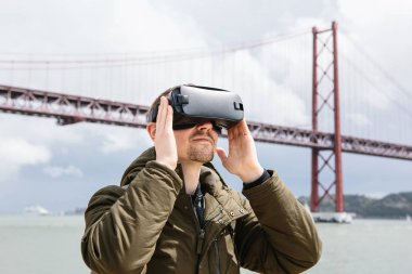 Bir adam sanal gerçeklik gözlük kullanır. 25 Nisan köprünün Lizbon içinde belgili tanımlık geçmiş. Sanal seyahat kavramı. Modern teknolojiler ve bunların kullanımı günlük yaşamda kavramı
