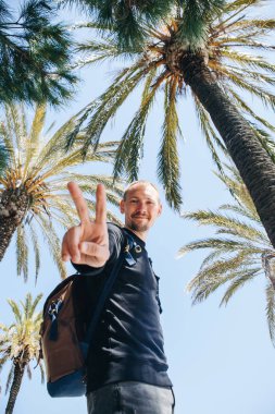 Pozitif genç bir adam, ya da mutlu bir turist veya palmiye ağaçları ve sıcak bir ülkede mavi gökyüzü arka plan üzerinde bir blogger