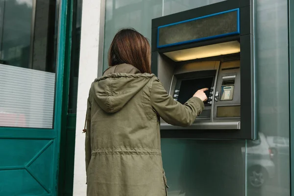 Una mujer joven toma dinero de un cajero automático. Toma una tarjeta del cajero automático. Finanzas, tarjeta de crédito, retiro de dinero . — Foto de Stock