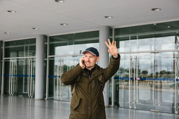 Un giovane turista di sesso maschile in aeroporto o vicino a un centro commerciale o stazione chiama un taxi o parla su un telefono cellulare o comunica con gli amici utilizzando un telefono cellulare — Foto Stock