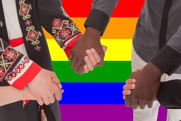 Menschen unterschiedlicher Nationalitäten halten sich vor dem Hintergrund der lgbt-Flagge die Hand — Stockfoto