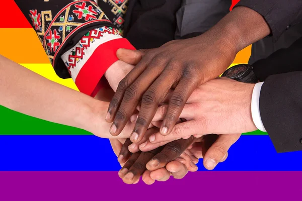 A különböző nemzetiségű emberek kéz a kézben a háttérben az LMBT lobogója — Stock Fotó