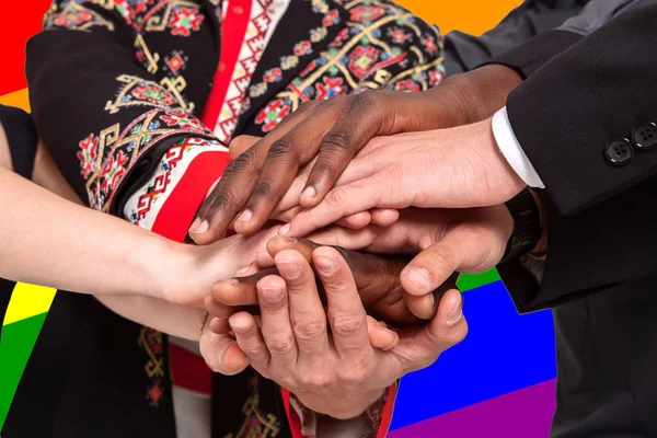 Menschen unterschiedlicher Nationalitäten halten sich vor dem Hintergrund der lgbt-Flagge die Hand — Stockfoto