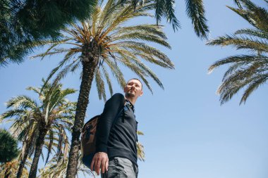 Pozitif genç bir adam, ya da mutlu bir turist veya palmiye ağaçları ve sıcak bir ülkede mavi gökyüzü arka plan üzerinde bir blogger