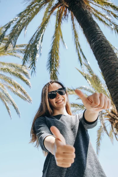 Jovencita positiva, o un turista feliz sobre un fondo de palmeras y cielo azul en un país caliente — Foto de Stock