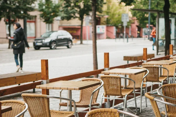 チェコ共和国プラハの通りカフェ。フォア グラウンドで空の木製のテーブルと籐の椅子があります。バック グラウンドでの都市生活がぼやけています。 — ストック写真