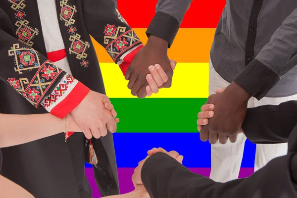 Pessoas de diferentes nacionalidades seguram as mãos contra o pano de fundo da bandeira LGBT — Fotografia de Stock