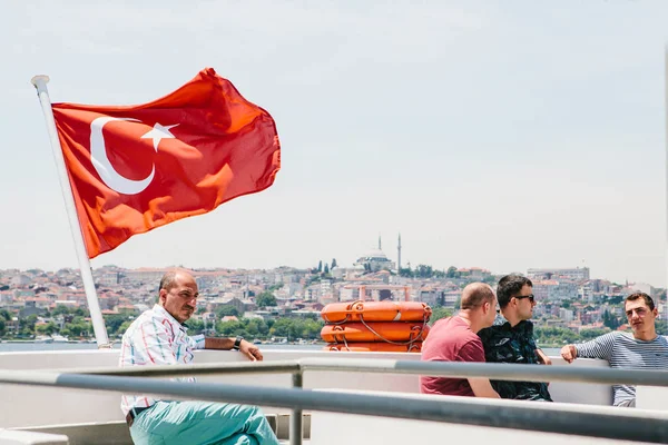 Estambul, 17 de junio de 2017: Los residentes locales se mueven en el agua en ferry o barco de pasajeros. Un hombre se sienta junto a la bandera turca. Cerca de un grupo de amigos se comunican y hablan . — Foto de Stock