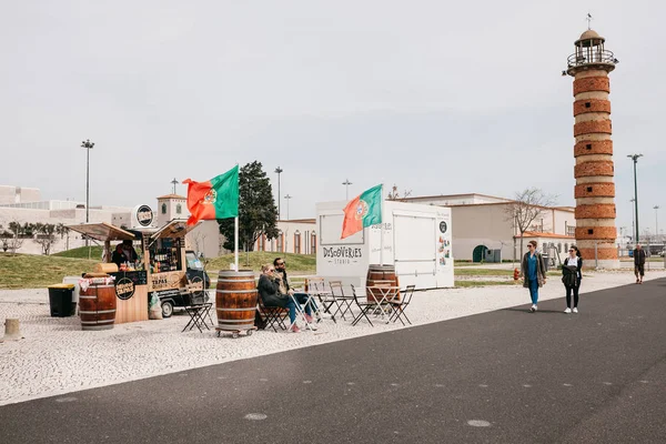 Lisbon, 18 Haziran 2018: Street ticarette Belem bölgesinde sahildeki yiyecek ve içecekler. Genç erkek ve kadın masada rahatlatıcı çift. Diğer insanlar etrafında yürüyor
