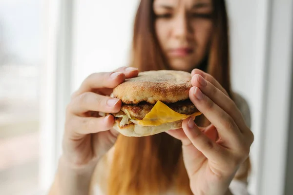 Una joven muestra que no le gusta una hamburguesa. Imagen conceptual del rechazo de una alimentación poco saludable . — Foto de Stock