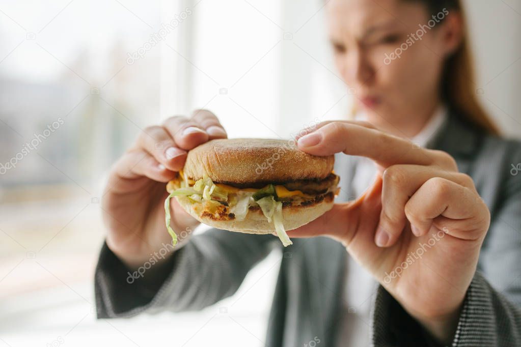 A young girl shows that she does not like a burger. Conceptual image of refusal from unhealthy eating.