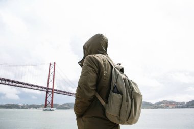 Genç bir seyahat veya bir turist Lizbon Portekiz Waterfront 25 Nisan köprünün yanındaki bir sırt çantası ile