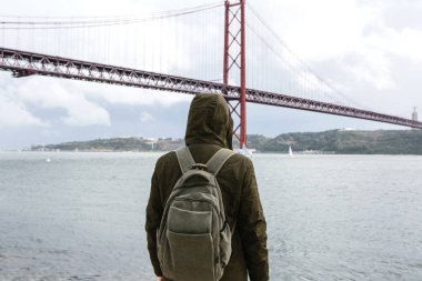 Genç bir seyahat veya bir turist Lizbon Portekiz Waterfront 25 Nisan köprünün yanındaki bir sırt çantası ile
