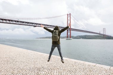 Genç bir seyahat veya bir turist Lizbon Portekiz Waterfront 25 Nisan köprünün yanındaki bir sırt çantası ile